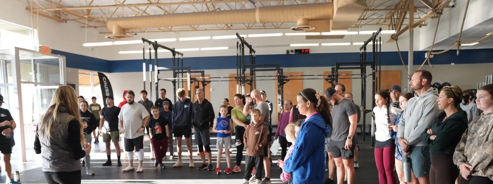 A coach briefs a full class of adults and kids before the workout